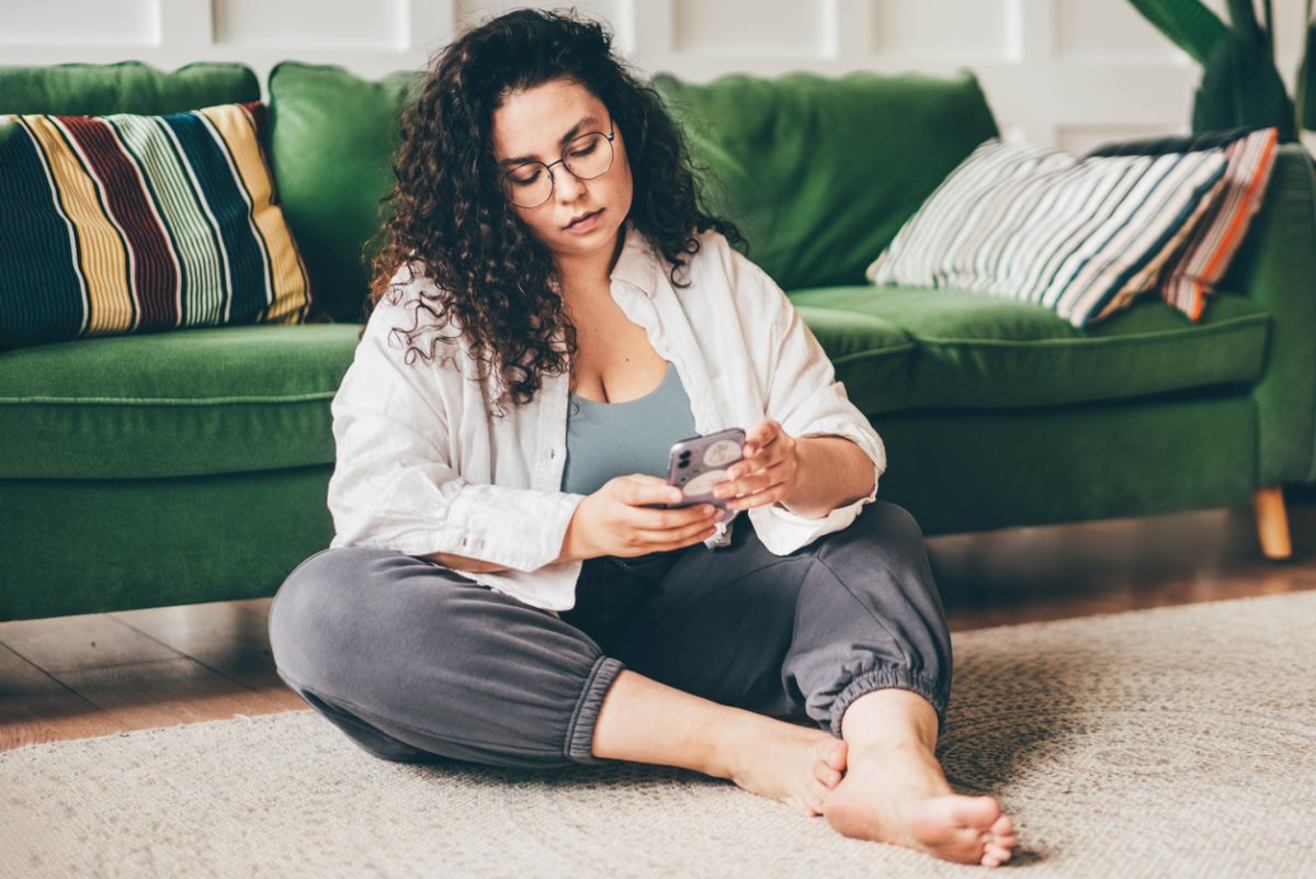  frau sitzt mit smartphone vor couch 
