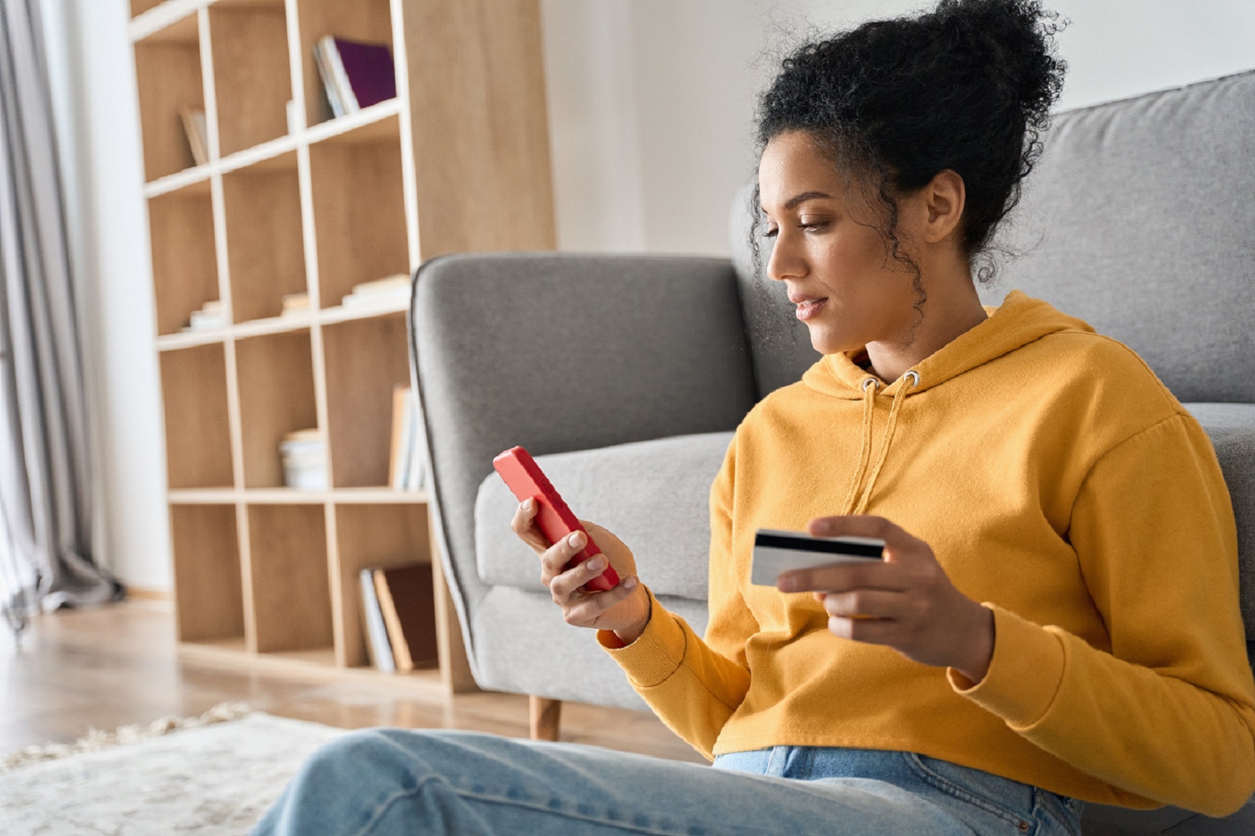  Eine junge Frau sitzt vor dem Sofa und zahlt online. 