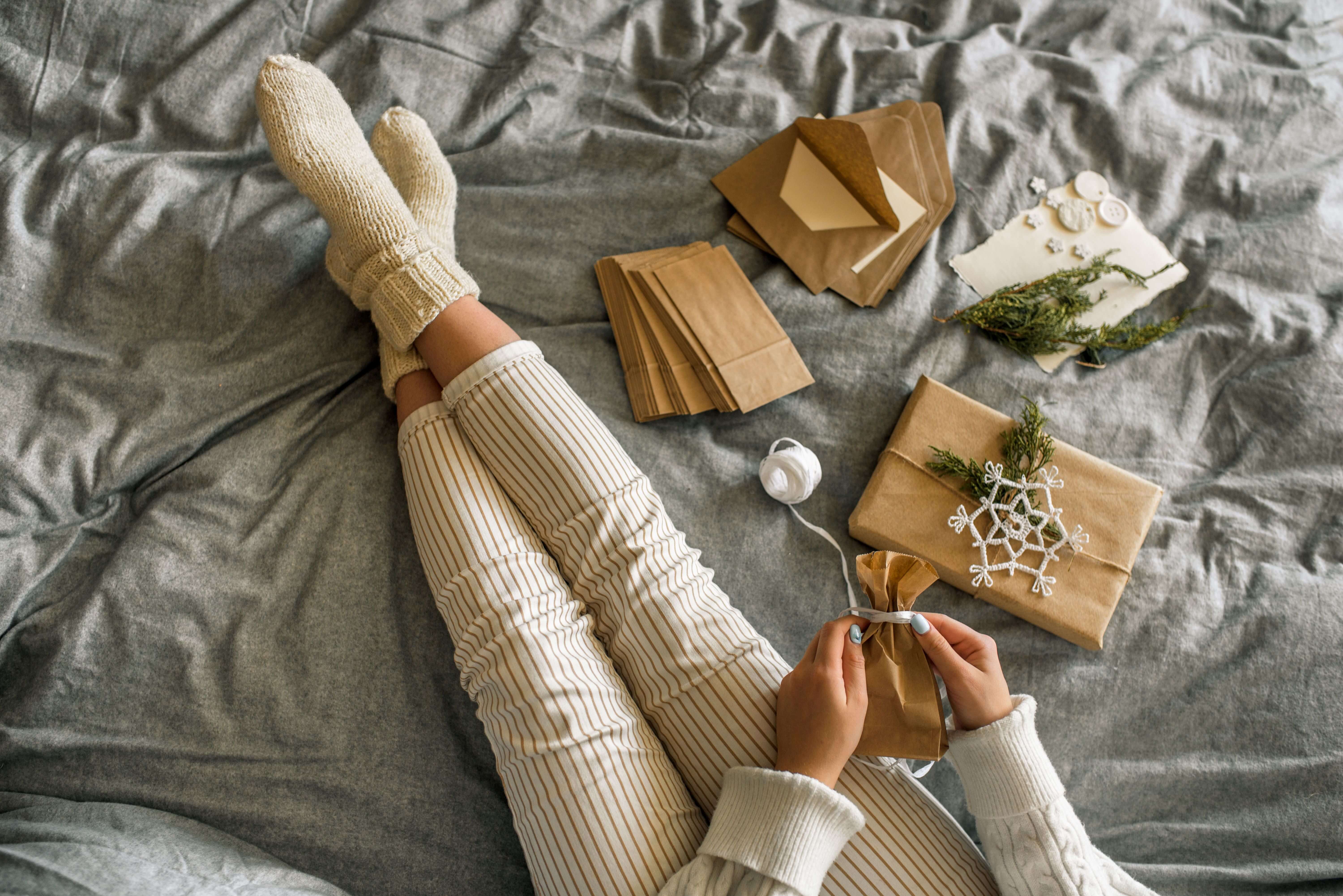  Frau sitzt auf Bett und packt Adventskalendergeschenke 