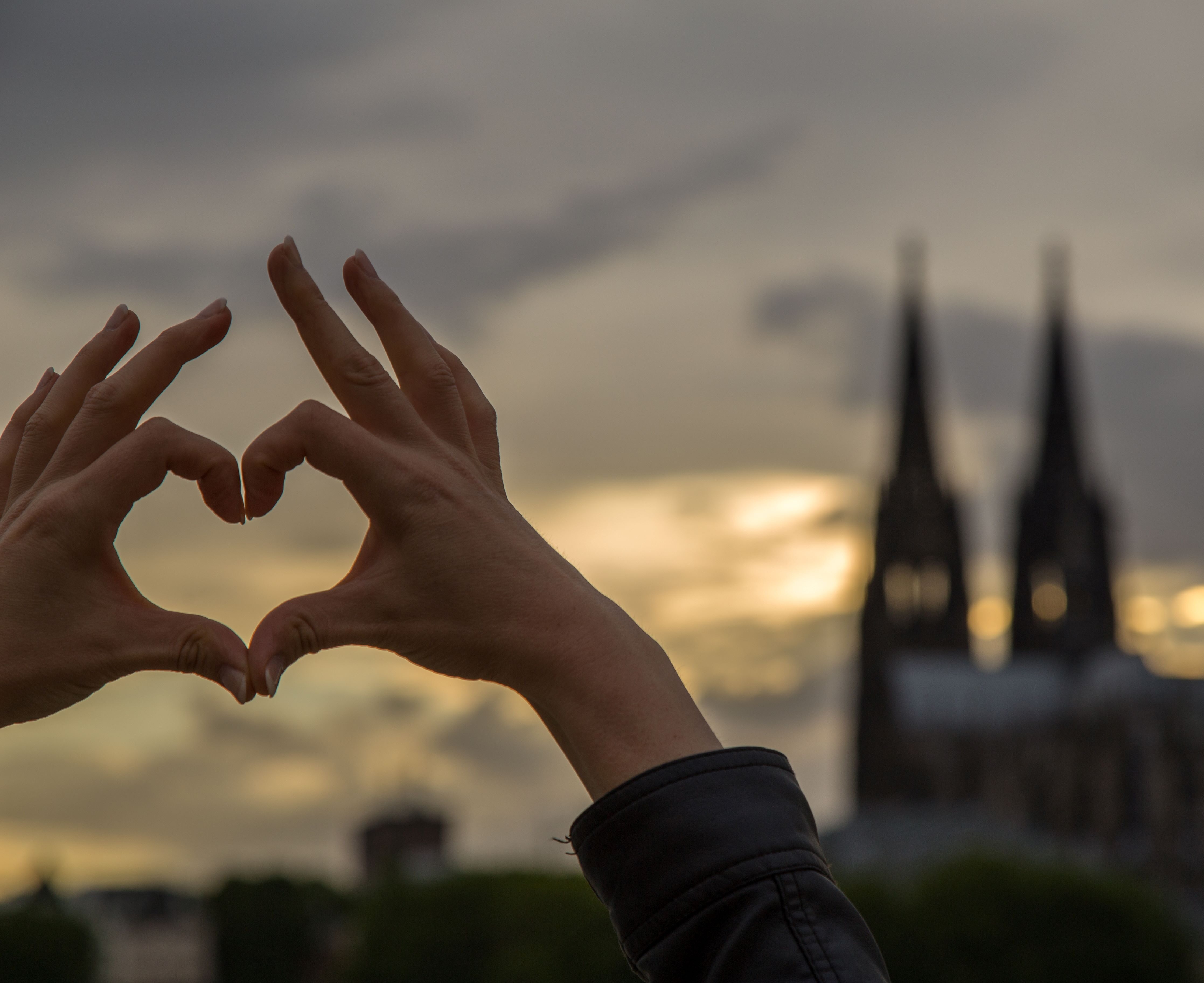  Person zeigt mit Händen ein Herzchen vor dem Kölner Dom 