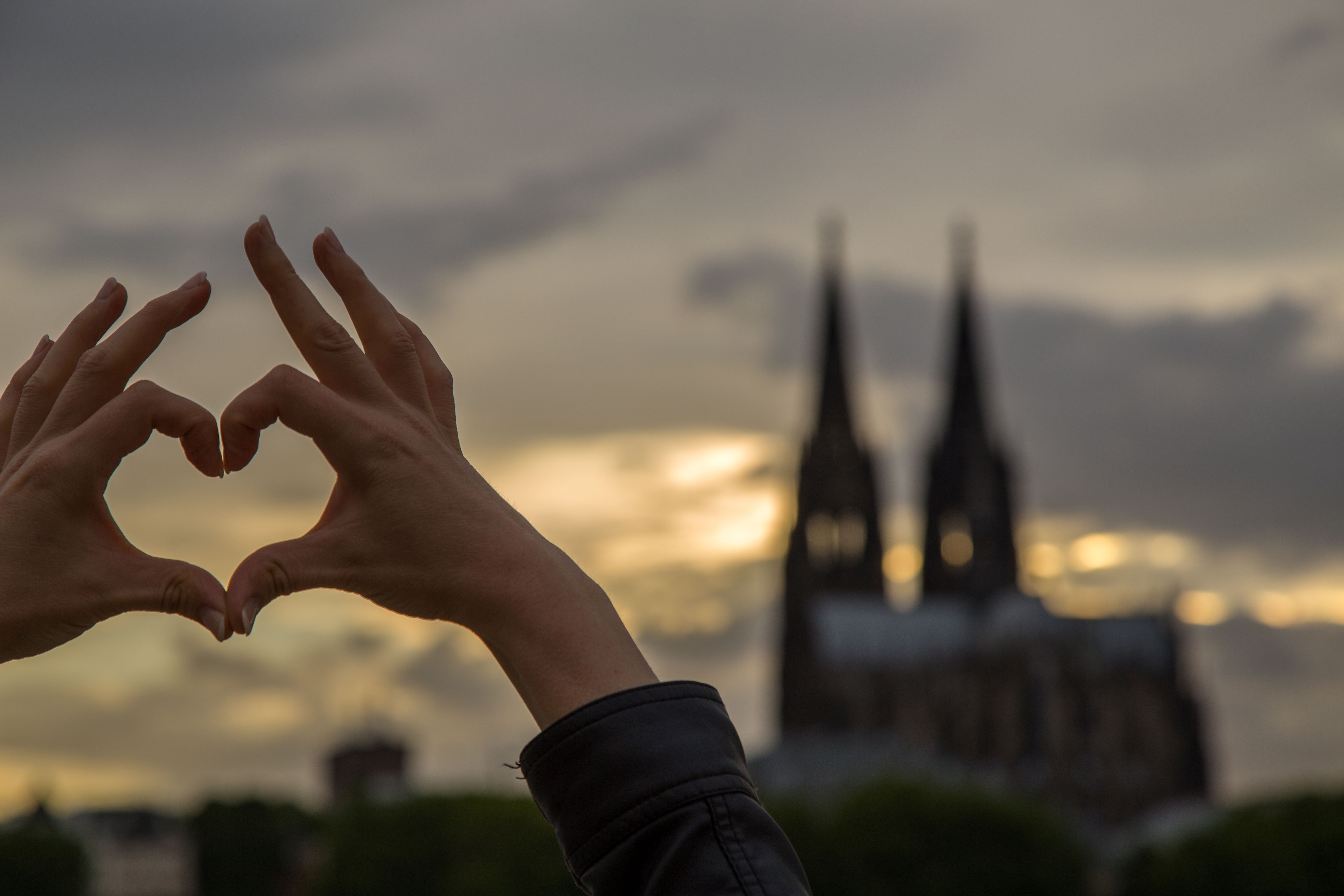  Person zeigt mit Händen ein Herzchen vor dem Kölner Dom 