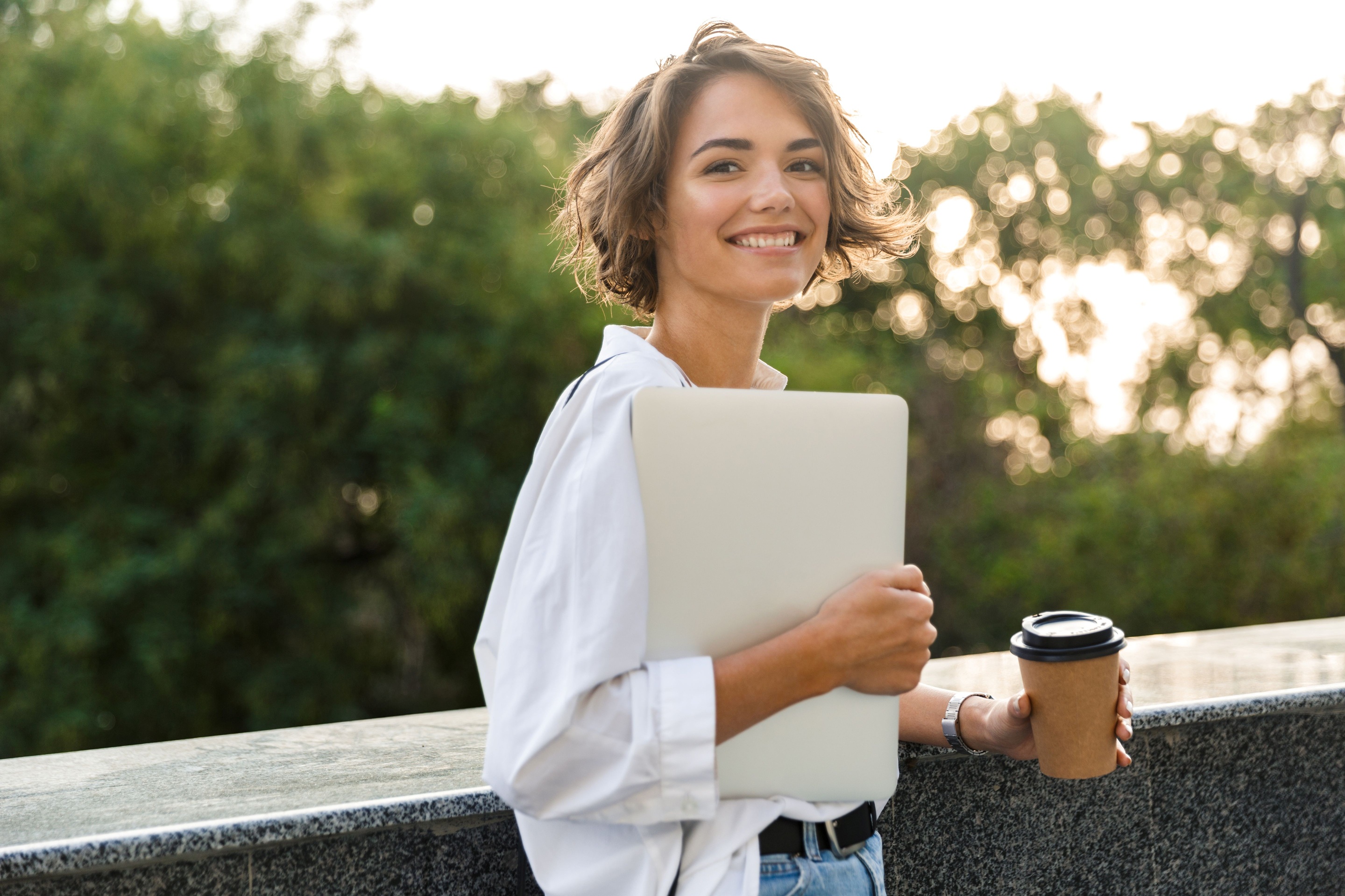 Frau mit Laptop und Kaffeebecher in der Hand