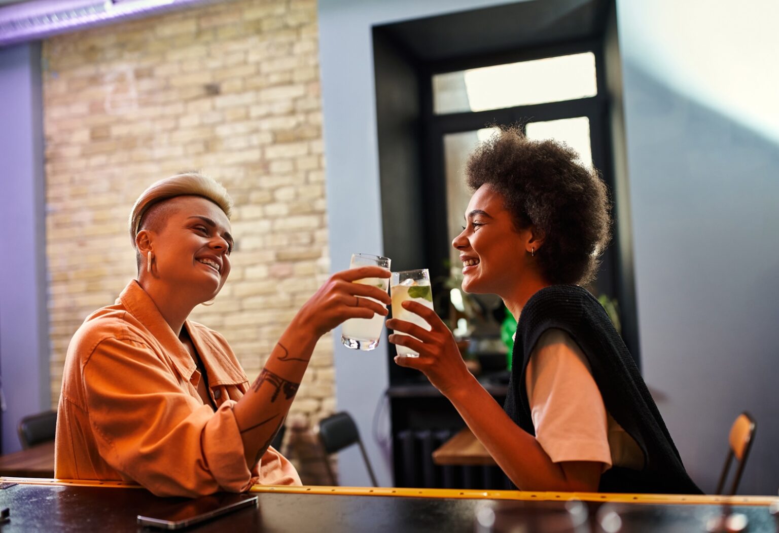  Zwei Frauen daten sich in einer Baar und stoßen mit ihrem Getränk an. 