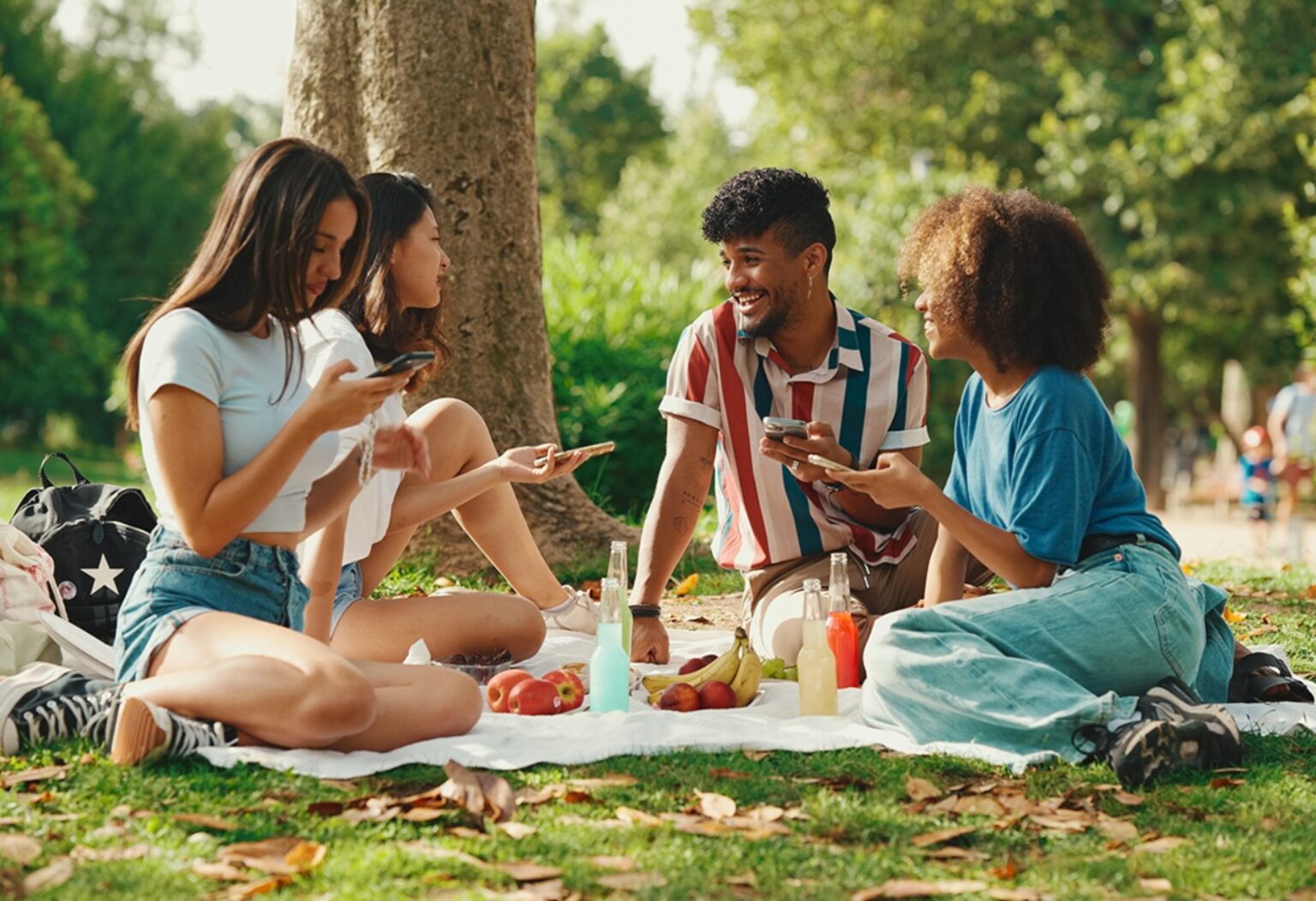 Freundesgruppe, die auf einer Picknickdecke im Park sitzt und gemeinsam isst und spricht.
