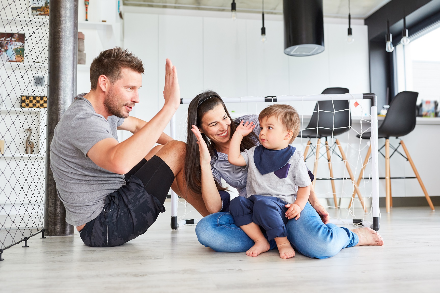  Eltern und Kind geben sich ein High Five im Wohnzimmer beim Spielen zusammen 