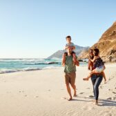 Auf dem Bild ist eine junge Familie mit zwei Kindern zu sehen, die an einem verlassenen Strand spazieren geht.