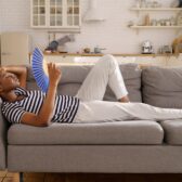 Eine Frau liegt auf einem Sofa und wedelt sich mit einem Fächer kühle Luft zu.