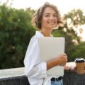 Frau mit Laptop und Kaffeebecher in der Hand