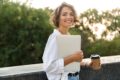 Frau mit Laptop und Kaffeebecher in der Hand