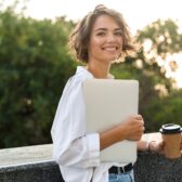 Frau mit Laptop und Kaffeebecher in der Hand