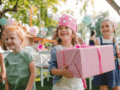 Drei kleine Mädchen auf einem Kindergeburtstag, eine von ihnen trägt eine gebastelte Krone und ein Geschenk