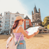 Eine Frau steht mit Stadtplan an der Rheinpromenade in Köln nahe den bunten Häusern