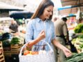 Eine Frau läuft mit einem Korb voll Gemüse über den Markt und schaut Gemüse an